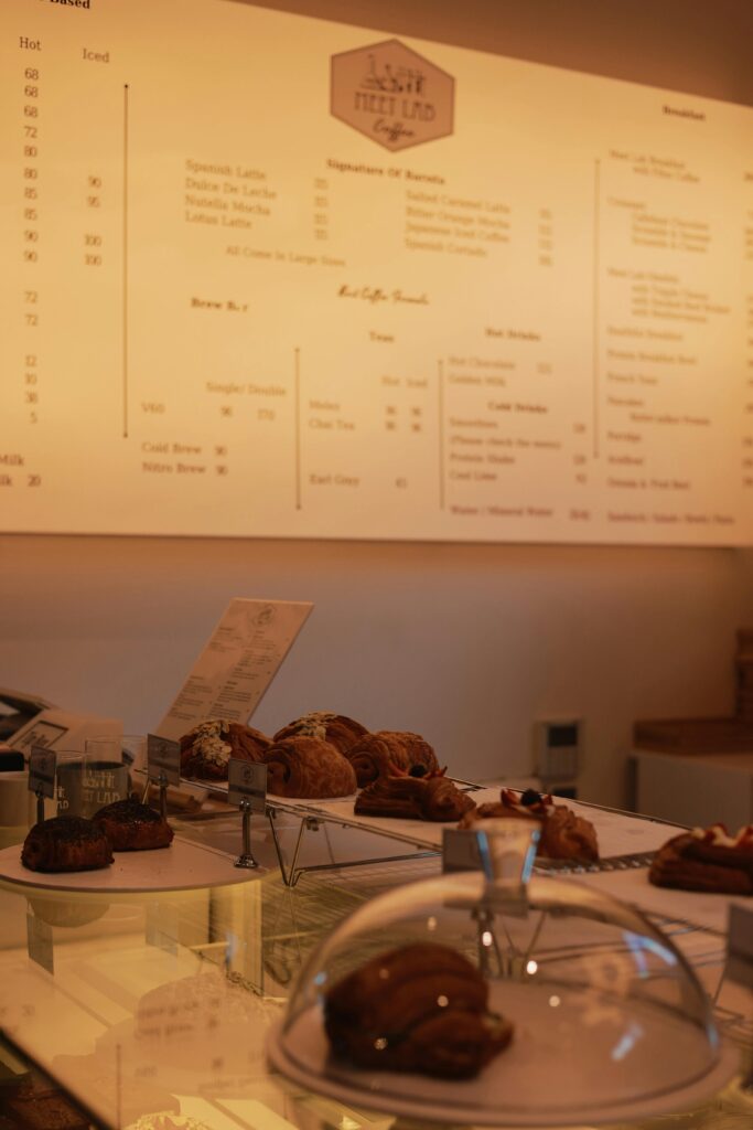 Warm ambient lighting highlights a café counter with pastries and menu board.