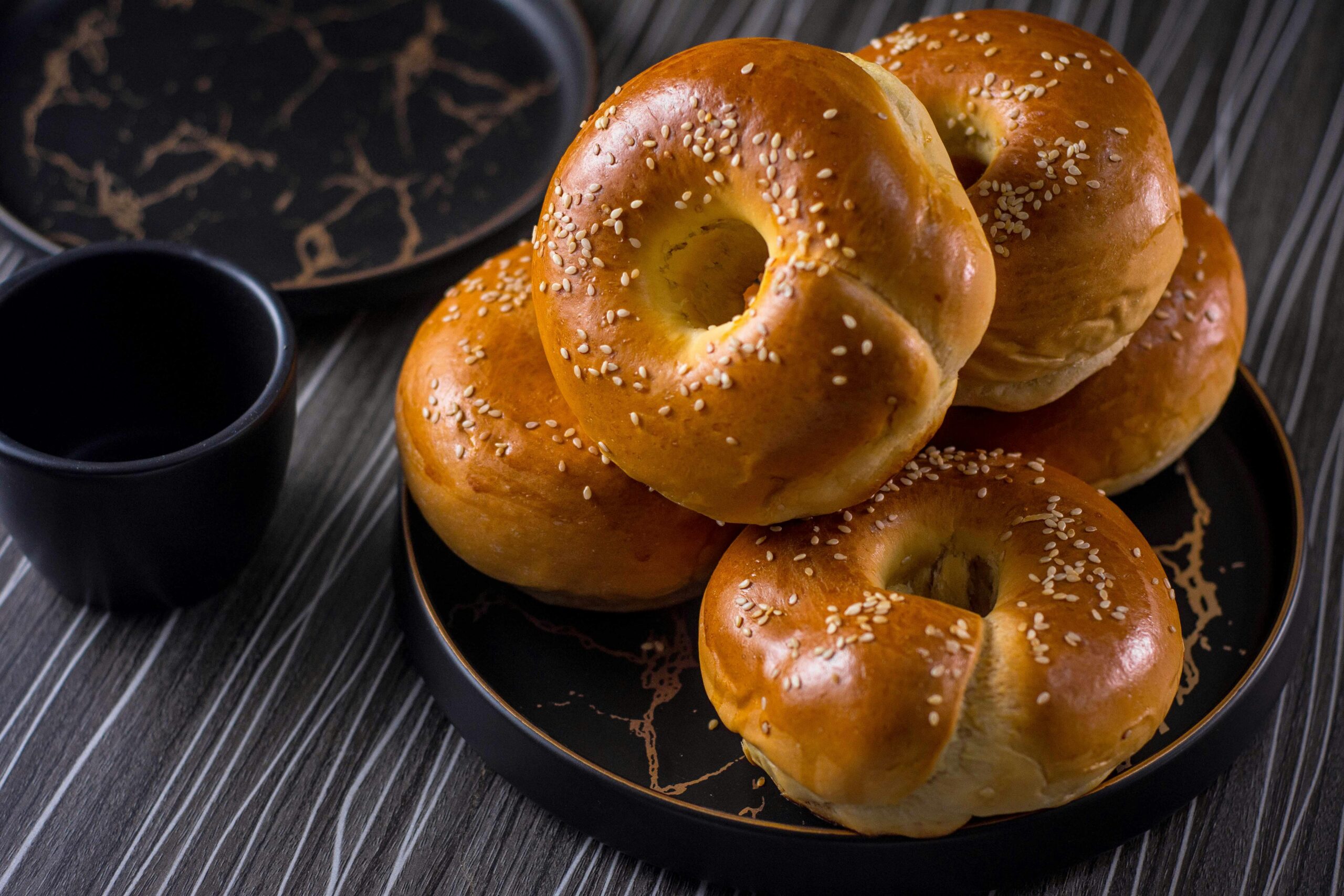 freshly baked sesame seed bagels on a stylish black plate.
