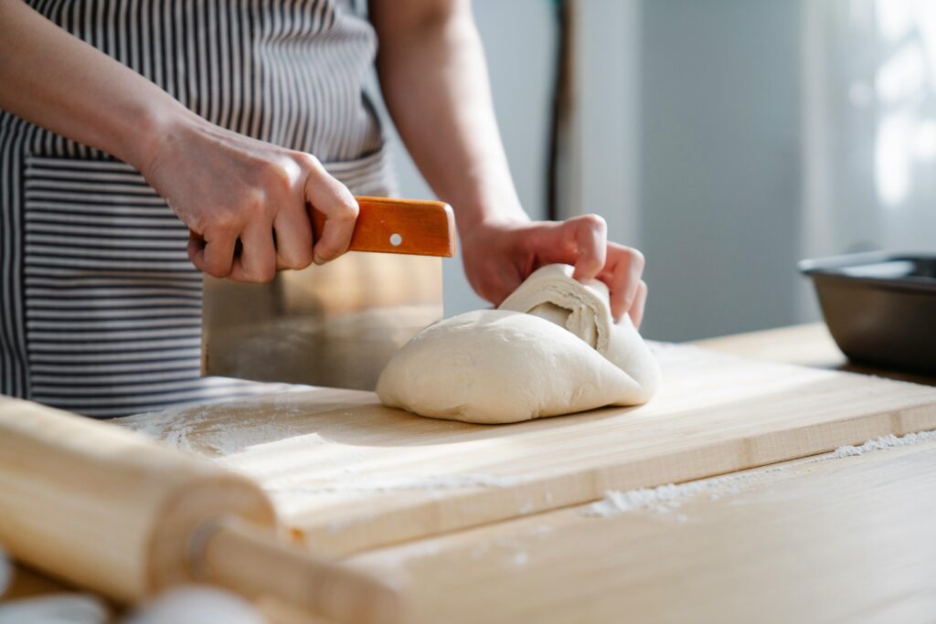 A close-up of hands slicing bread dough on a floured wooden board, capturing the baking process.